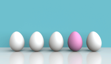 4 white eggs lines up with 1 stand out pink egg on blue background